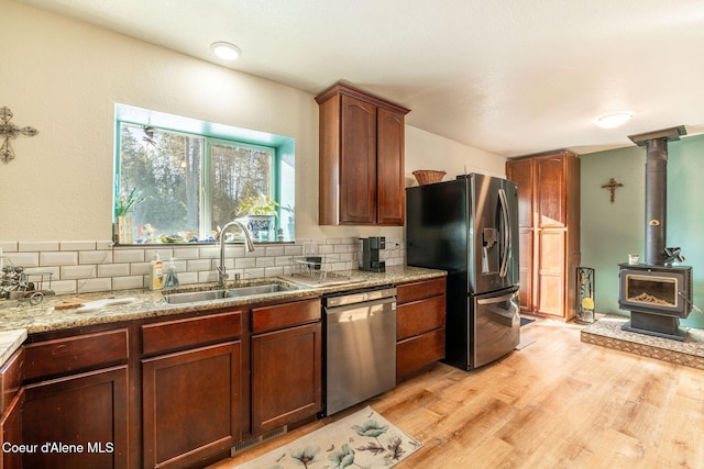 kitchen featuring sink, light stone counters, light wood-type flooring, appliances with stainless steel finishes, and decorative backsplash