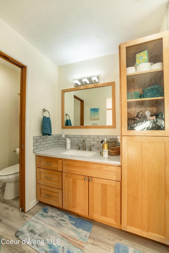 bathroom with wood-type flooring, vanity, backsplash, and toilet