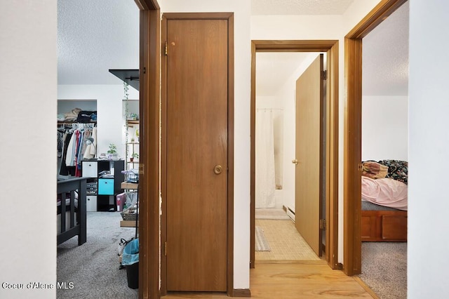 hallway with light colored carpet, a baseboard radiator, and a textured ceiling