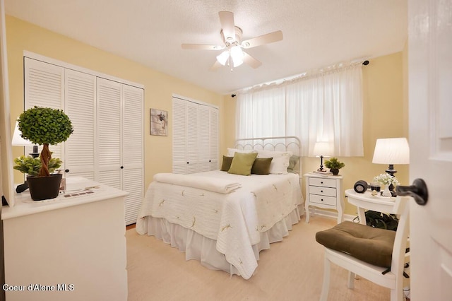 bedroom with two closets, light colored carpet, and ceiling fan