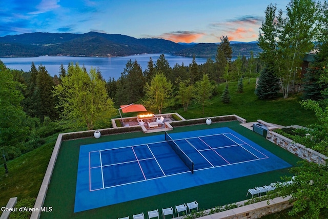 view of tennis court featuring an outdoor fire pit and a water and mountain view