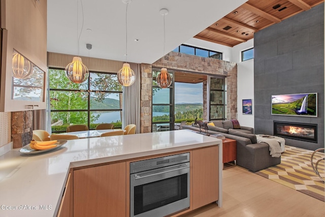 kitchen with pendant lighting, a tiled fireplace, stainless steel oven, wood ceiling, and light wood-type flooring