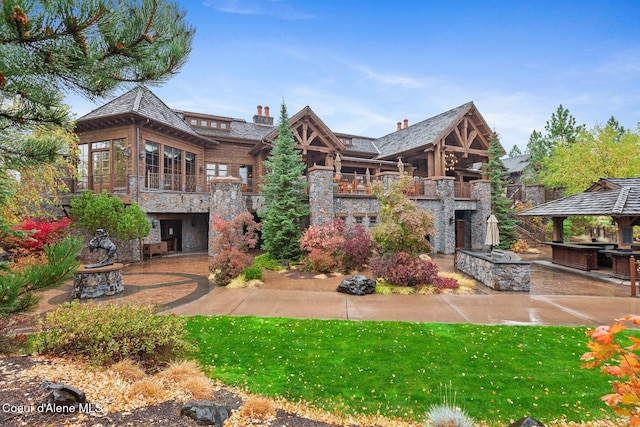 rear view of property featuring a gazebo, a yard, and an outdoor stone fireplace