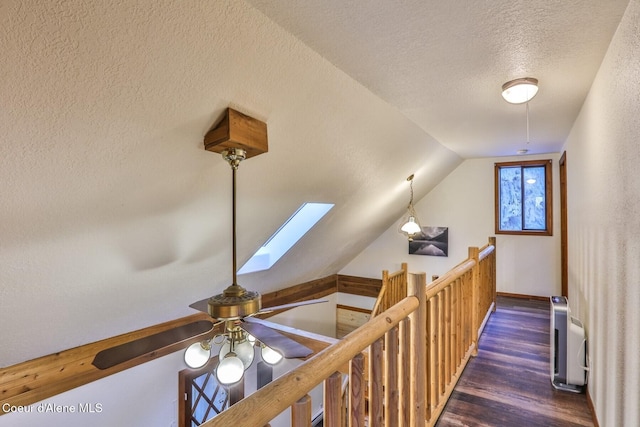 hallway featuring dark wood-type flooring, vaulted ceiling with skylight, and a textured ceiling