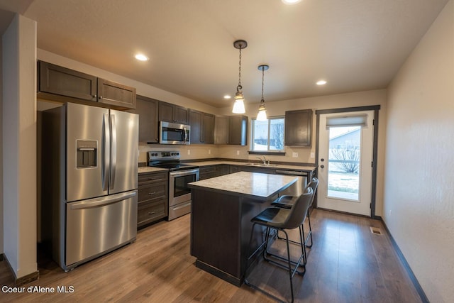 kitchen featuring pendant lighting, a breakfast bar area, dark brown cabinets, stainless steel appliances, and a center island