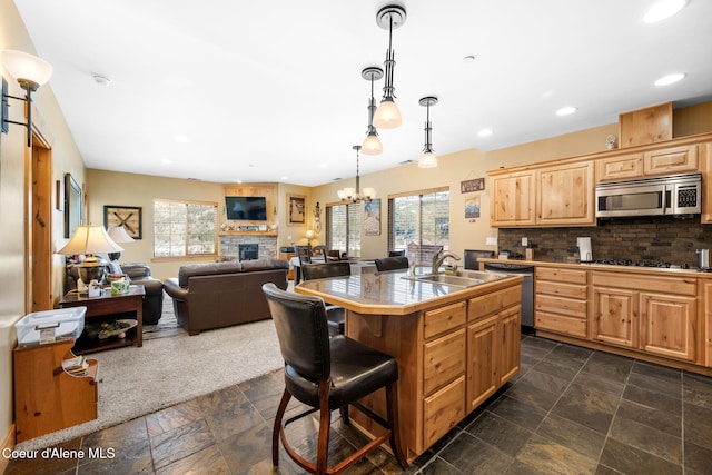 kitchen with sink, backsplash, hanging light fixtures, a kitchen island with sink, and stainless steel appliances