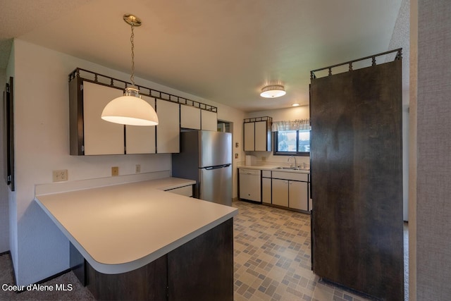 kitchen featuring pendant lighting, sink, stainless steel refrigerator, white dishwasher, and kitchen peninsula