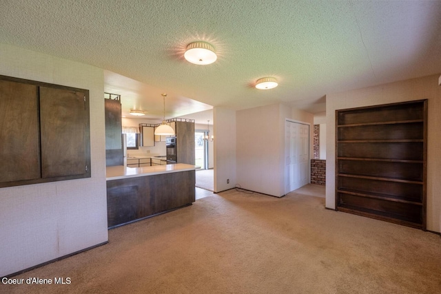 kitchen with pendant lighting, light carpet, kitchen peninsula, and a textured ceiling