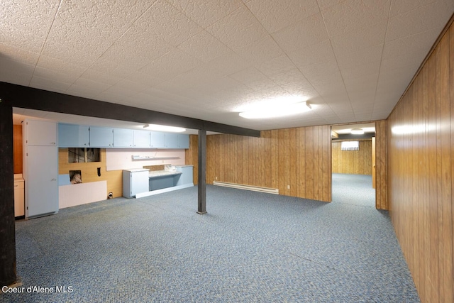 basement with a baseboard heating unit, dark carpet, and wooden walls