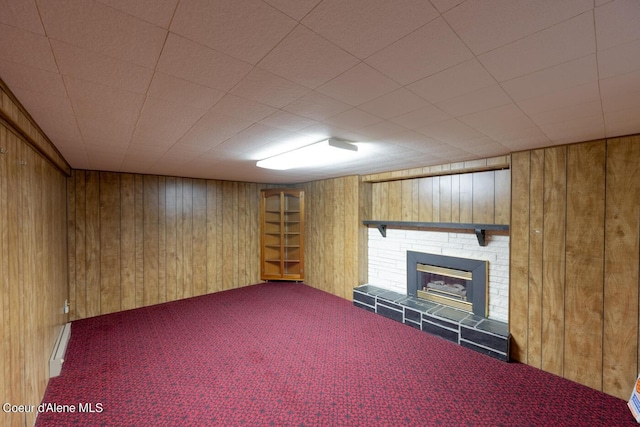 basement featuring a tiled fireplace, wood walls, and carpet flooring