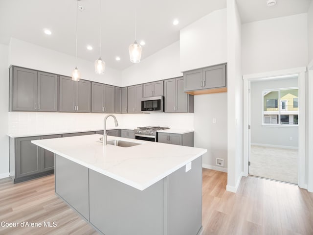 kitchen with sink, hanging light fixtures, appliances with stainless steel finishes, light stone countertops, and a kitchen island with sink