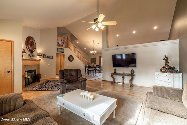 living room with ceiling fan with notable chandelier, high vaulted ceiling, a tile fireplace, and light wood-type flooring