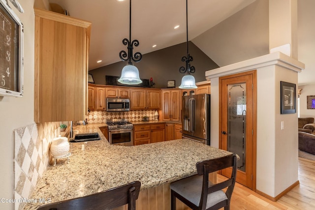 kitchen with sink, high end appliances, hanging light fixtures, light wood-type flooring, and decorative backsplash