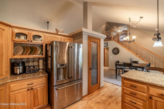 kitchen featuring high vaulted ceiling, decorative light fixtures, high end refrigerator, light stone counters, and light hardwood / wood-style flooring