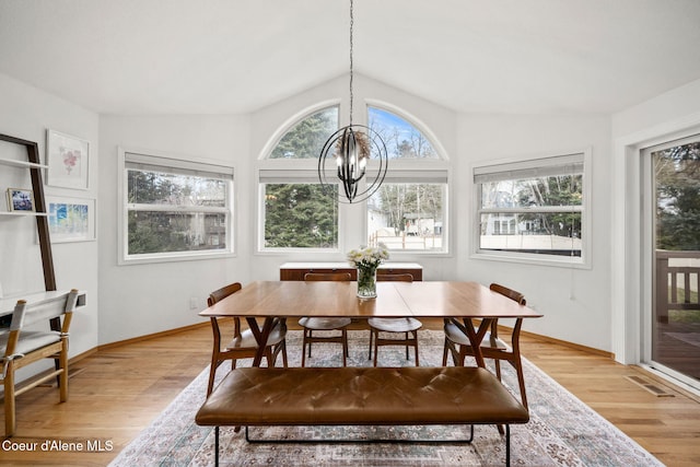 dining space with vaulted ceiling, plenty of natural light, an inviting chandelier, and light hardwood / wood-style flooring