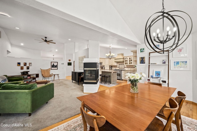 dining room featuring ceiling fan with notable chandelier, light hardwood / wood-style floors, and vaulted ceiling