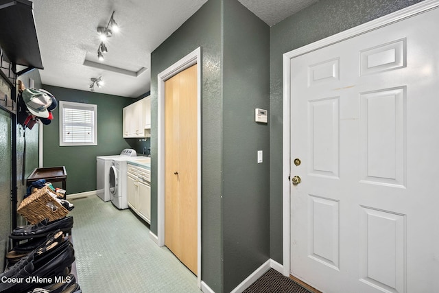 clothes washing area with cabinets, rail lighting, a textured ceiling, and washing machine and clothes dryer