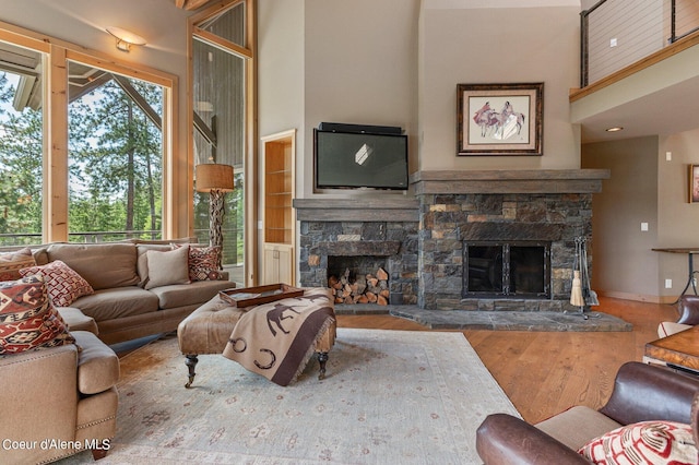 living room with hardwood / wood-style flooring, a stone fireplace, and a high ceiling