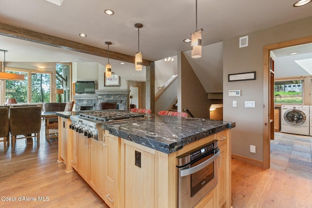 kitchen with appliances with stainless steel finishes, a kitchen island, light brown cabinetry, a stone fireplace, and light wood-type flooring