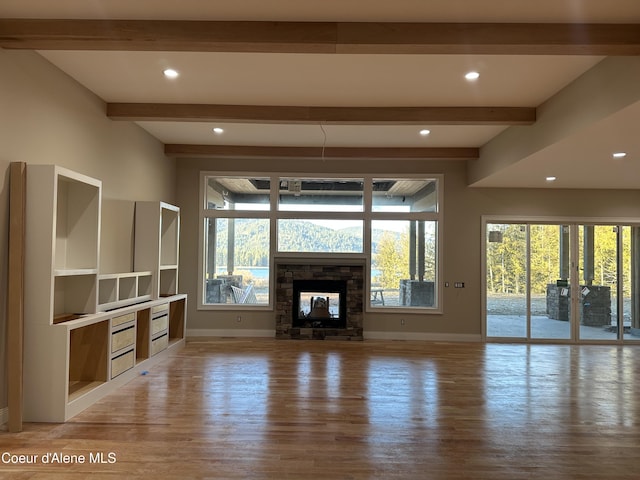 unfurnished living room with beamed ceiling, a stone fireplace, and light hardwood / wood-style flooring