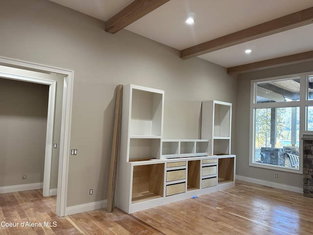 interior space featuring beamed ceiling, a stone fireplace, and light wood-type flooring