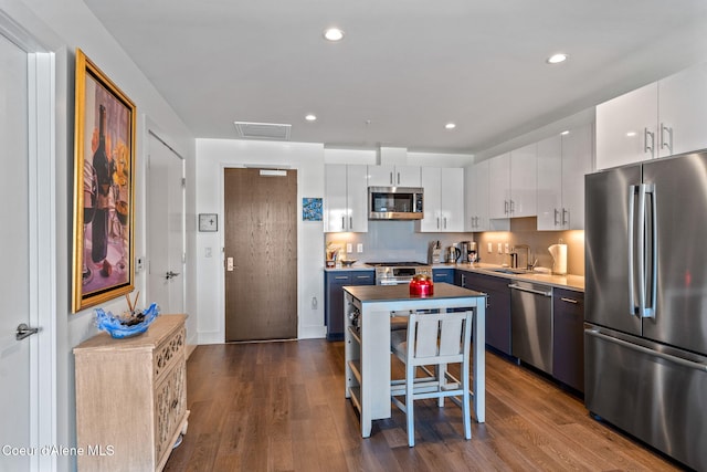 kitchen with sink, stainless steel appliances, white cabinets, a kitchen island, and dark hardwood / wood-style flooring