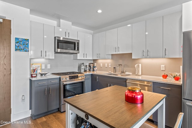 kitchen with gray cabinets, white cabinetry, sink, light hardwood / wood-style floors, and stainless steel appliances