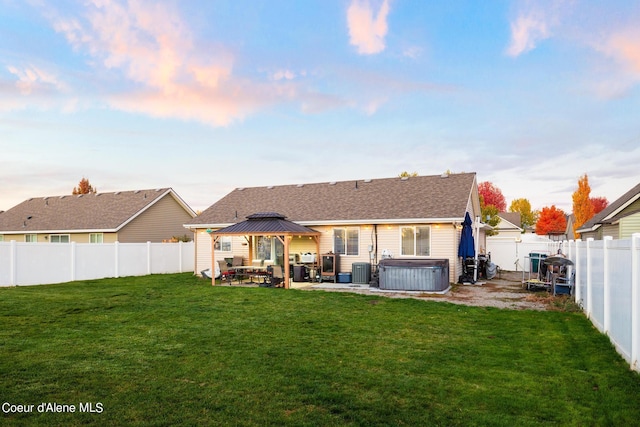 back house at dusk featuring a gazebo, a hot tub, a patio area, and a lawn