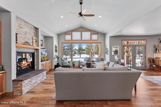 living room featuring french doors, a stone fireplace, high vaulted ceiling, light hardwood / wood-style flooring, and ceiling fan