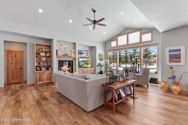 living room with built in shelves, a stone fireplace, high vaulted ceiling, and light wood-type flooring