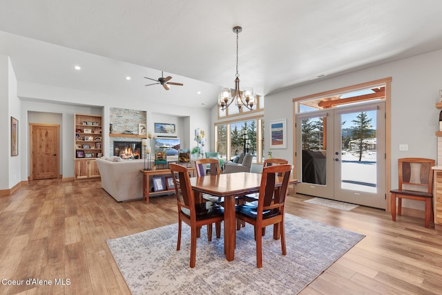 dining room with vaulted ceiling, a stone fireplace, built in shelves, light wood-type flooring, and french doors