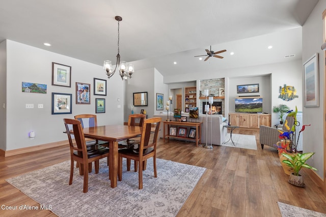 dining space featuring a fireplace, ceiling fan with notable chandelier, built in features, and light wood-type flooring