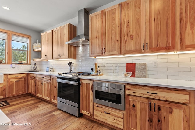 kitchen with light hardwood / wood-style flooring, wall chimney range hood, backsplash, and stainless steel gas range