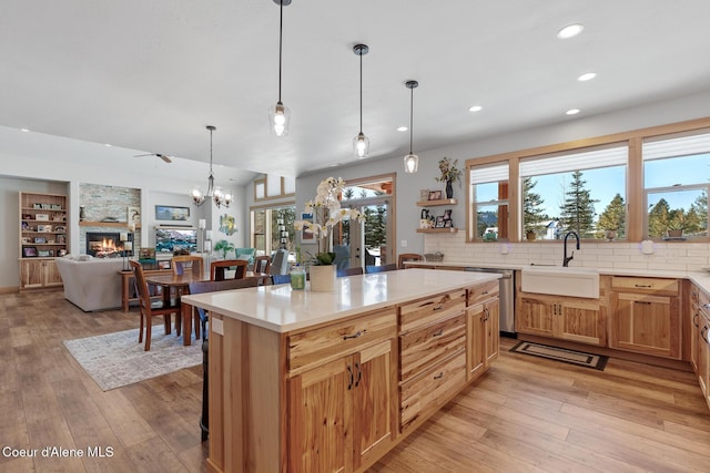 kitchen featuring a kitchen island, pendant lighting, sink, stainless steel dishwasher, and light hardwood / wood-style floors