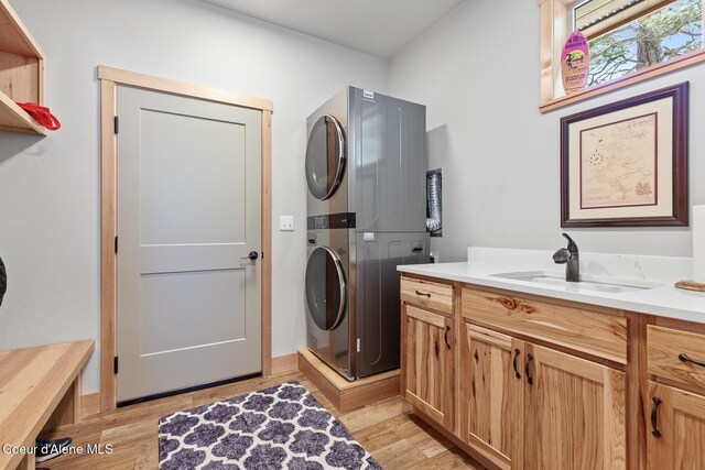 laundry area featuring sink, light hardwood / wood-style floors, cabinets, and stacked washer / dryer