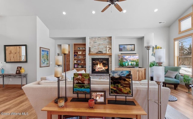 living room featuring built in features, a fireplace, light hardwood / wood-style floors, and ceiling fan