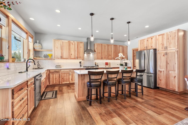 kitchen featuring wall chimney exhaust hood, a center island, hanging light fixtures, light hardwood / wood-style flooring, and appliances with stainless steel finishes