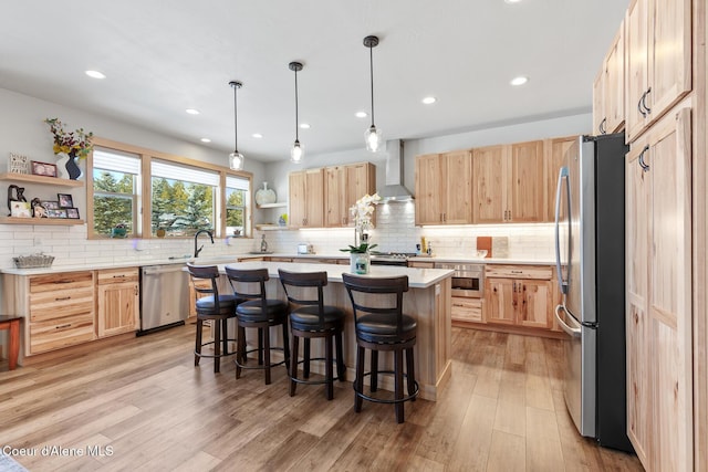 kitchen with light brown cabinetry, wall chimney range hood, a kitchen island, and appliances with stainless steel finishes