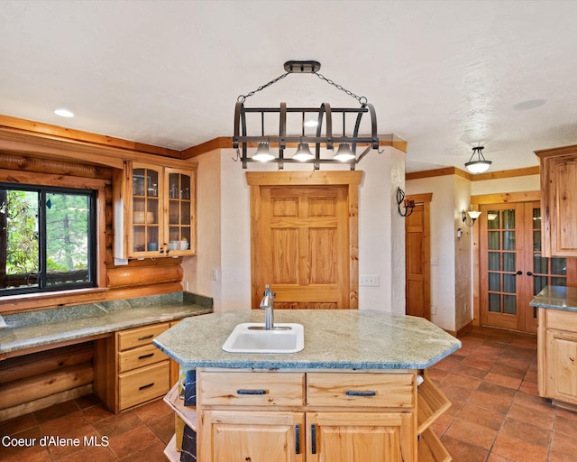 kitchen with light brown cabinetry, sink, light stone counters, a center island with sink, and pendant lighting