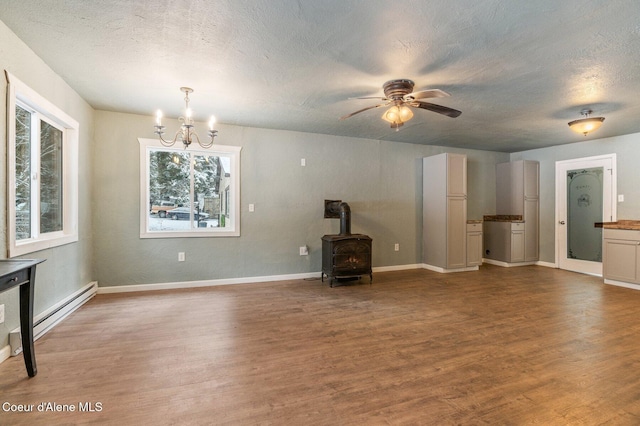 unfurnished living room with a textured ceiling, wood-type flooring, baseboard heating, and a wood stove