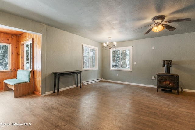 unfurnished living room with a baseboard heating unit, hardwood / wood-style flooring, wooden walls, and a wood stove