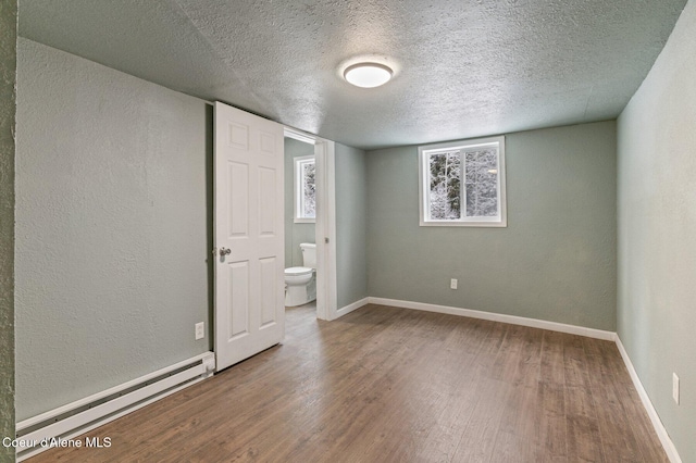 unfurnished bedroom featuring connected bathroom, a baseboard heating unit, hardwood / wood-style flooring, and a textured ceiling