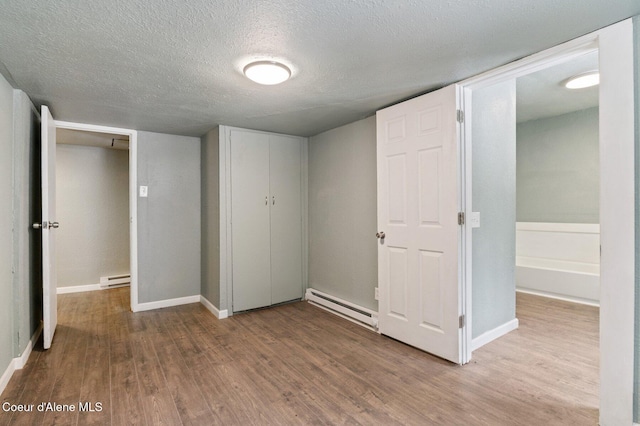 unfurnished bedroom featuring hardwood / wood-style flooring, a closet, a textured ceiling, and a baseboard heating unit