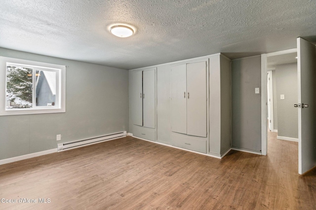 unfurnished bedroom featuring a baseboard heating unit, hardwood / wood-style floors, a textured ceiling, and a closet