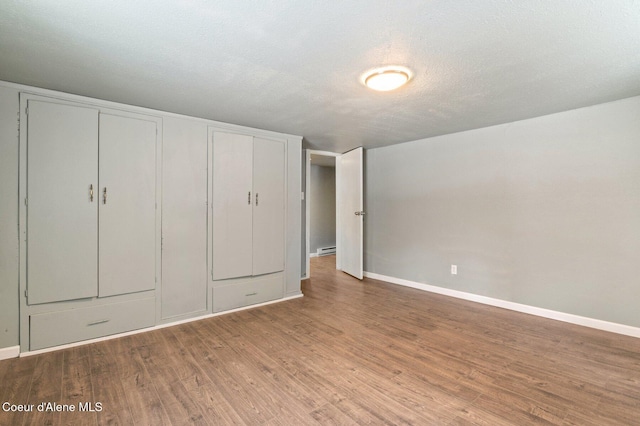 unfurnished bedroom featuring hardwood / wood-style flooring, a textured ceiling, and baseboard heating