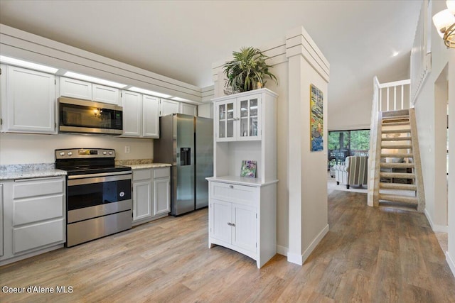 kitchen featuring stainless steel appliances, light stone counters, white cabinets, and light wood-type flooring