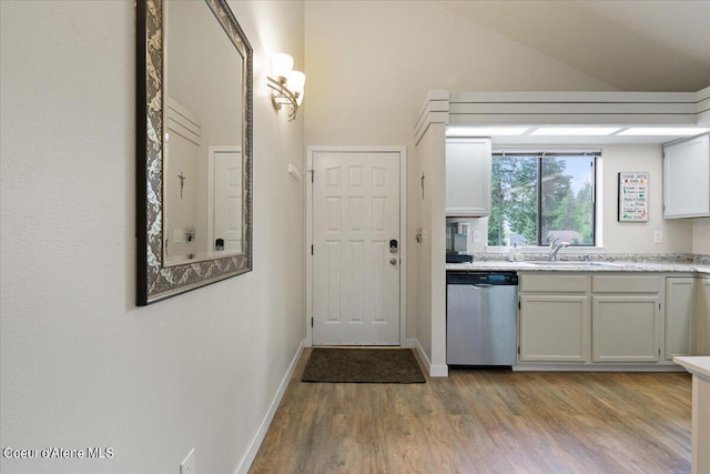 kitchen featuring sink, white cabinetry, vaulted ceiling, light wood-type flooring, and dishwasher