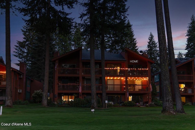 back house at dusk featuring a balcony and a lawn