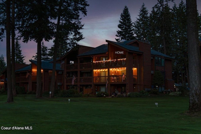 back house at dusk with a yard and a balcony