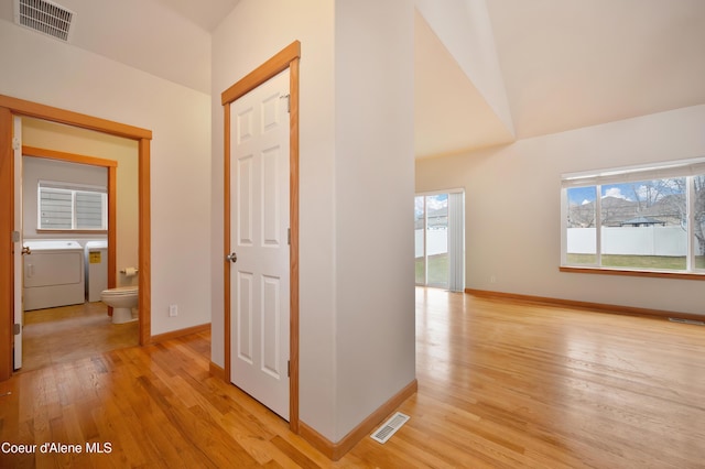 hallway with vaulted ceiling, light wood-type flooring, and washer and clothes dryer